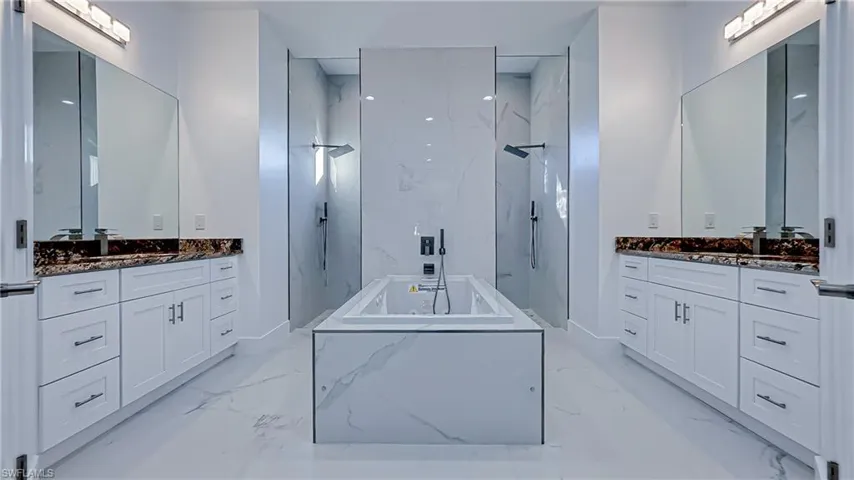 Bathroom with a marble finish shower, a garden tub, two vanities, and stone wall