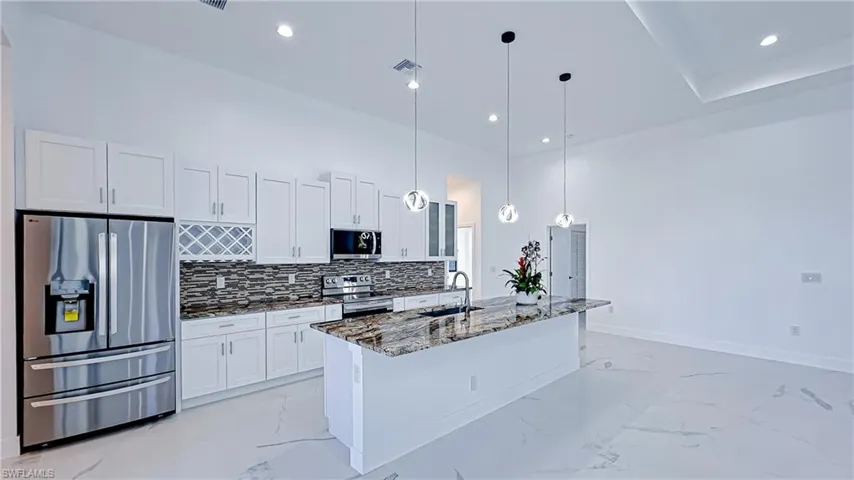 Kitchen with stainless steel appliances, dark stone countertops, hanging light fixtures, white cabinets, and a center island with sink