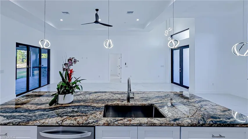Kitchen featuring dark stone countertops, decorative light fixtures, white cabinetry, and a raised ceiling