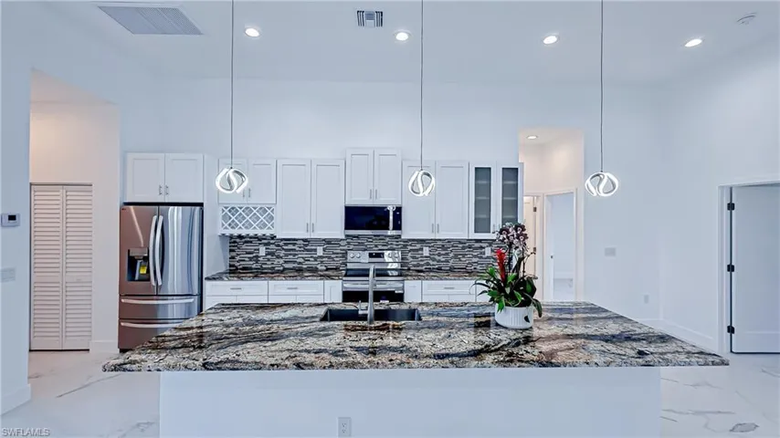 Kitchen featuring glass insert cabinets, dark stone countertops, stainless steel appliances, a high ceiling, and hanging light fixtures