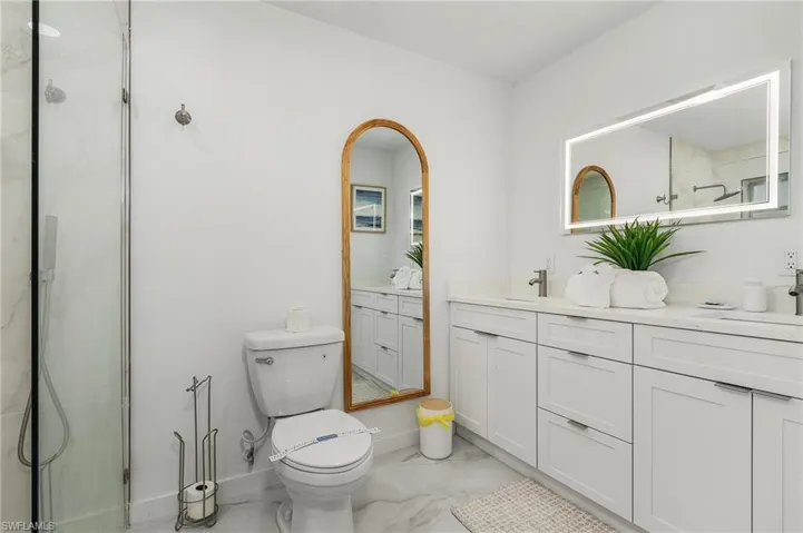 Full bathroom featuring marble look tile flooring, double vanity, toilet, a shower, and baseboards