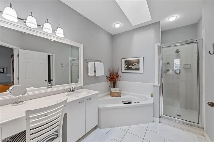 Bathroom featuring a bath, light tile patterned flooring, a skylight, vanity, and a shower stall