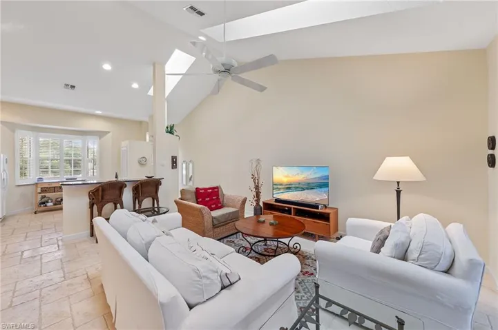 Living room featuring a skylight, stone tile flooring, high vaulted ceiling, recessed lighting, and ceiling fan