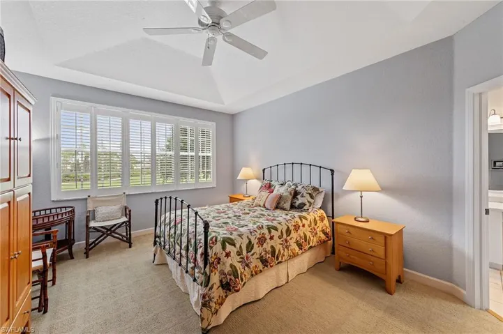 Bedroom with a tray ceiling, light colored carpet, a ceiling fan, and a textured wall