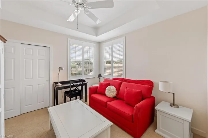 Living area featuring light colored carpet, a ceiling fan, and a raised ceiling