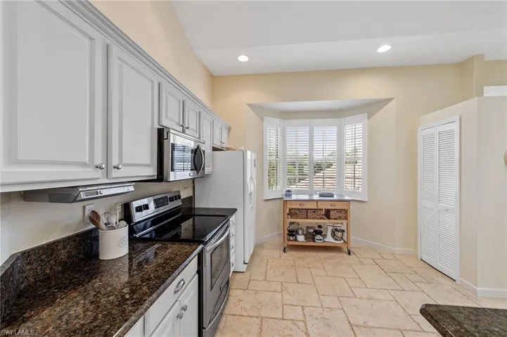 Kitchen featuring stainless steel appliances, dark stone countertops, stone tile floors, recessed lighting, and white cabinetry