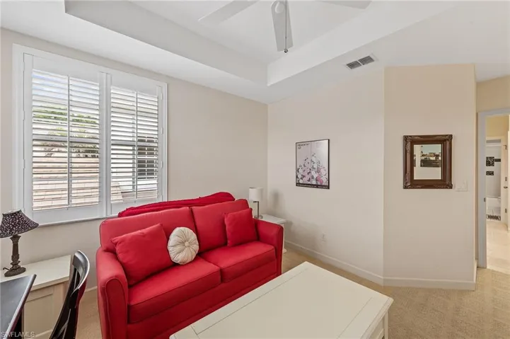 Living area featuring a raised ceiling, light colored carpet, and ceiling fan