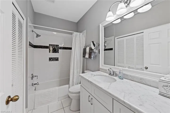 Bathroom featuring a closet, shower / tub combo with curtain, vanity, and light tile patterned floors