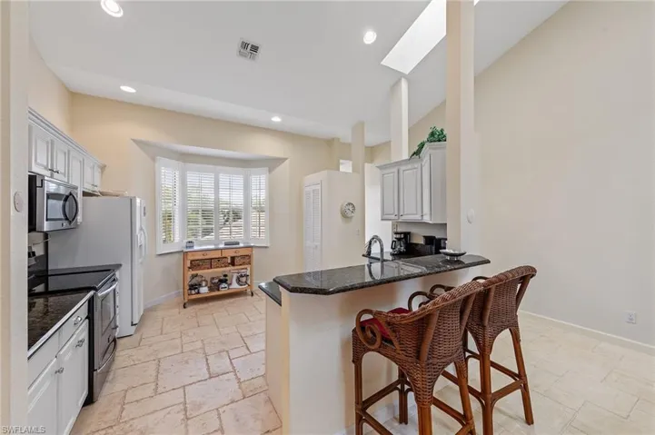 Kitchen with stainless steel appliances, a breakfast bar, a skylight, dark stone counters, and a peninsula