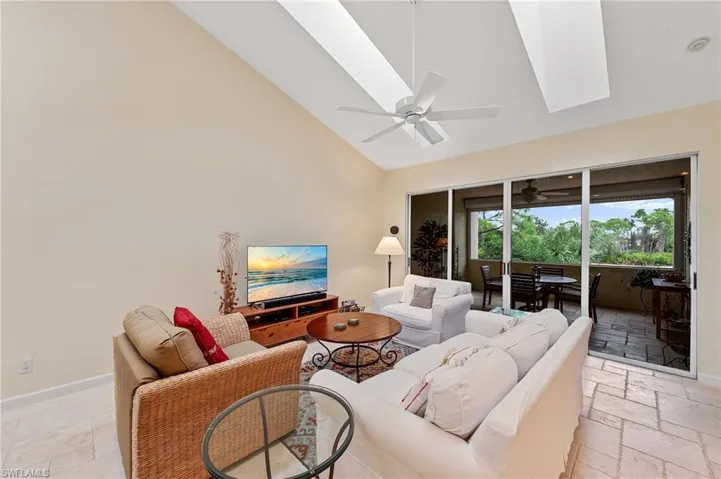 Living area featuring high vaulted ceiling, stone tile floors, a skylight, a ceiling fan, and a sunroom