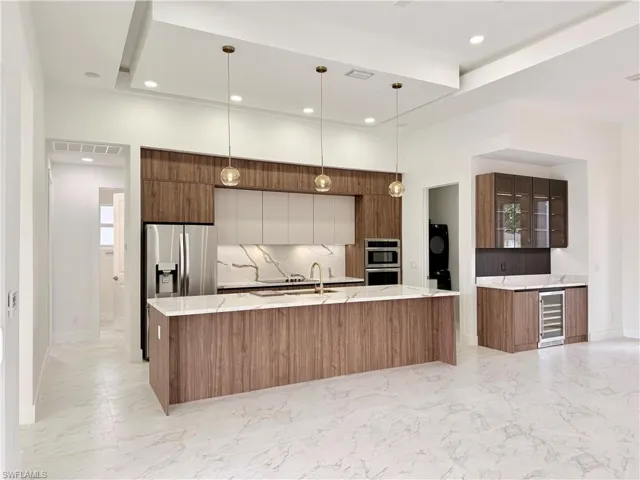 Kitchen with modern cabinets, appliances with stainless steel finishes, light marble finish flooring, wine cooler, and backsplash