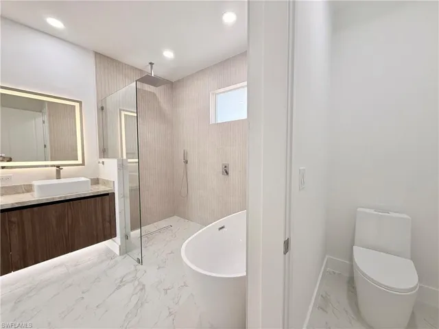 Bathroom with marble finish flooring, tiled shower, vanity, a soaking tub, and recessed lighting