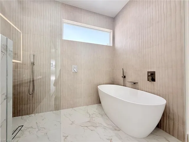 Full bath with a freestanding bath, walk in shower, marble tiled floors, and tile walls