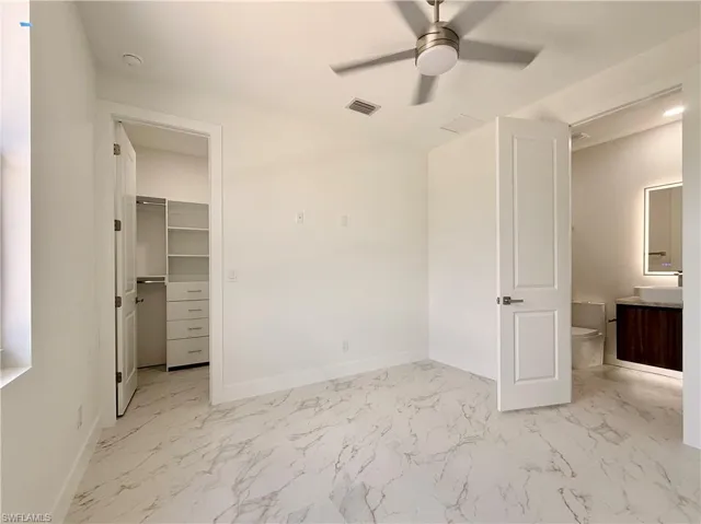 Unfurnished bedroom with light marble finish floors, a spacious closet, a ceiling fan, a closet, and ensuite bathroom