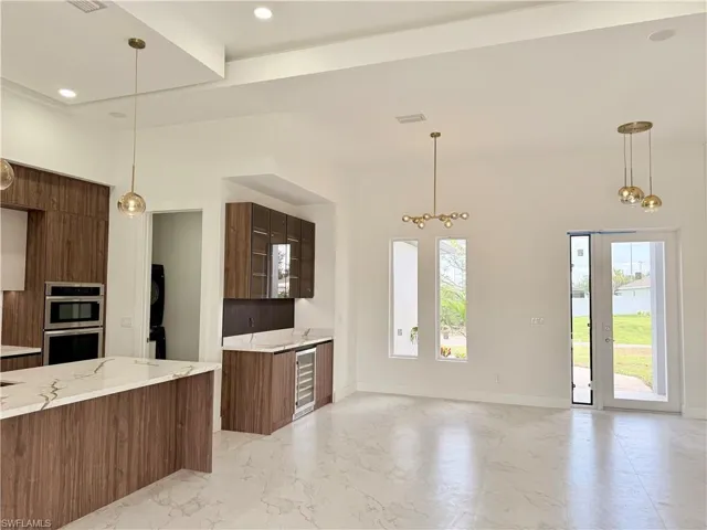 Kitchen featuring modern cabinets, beverage cooler, stainless steel double oven, hanging light fixtures, and light marble finish floors
