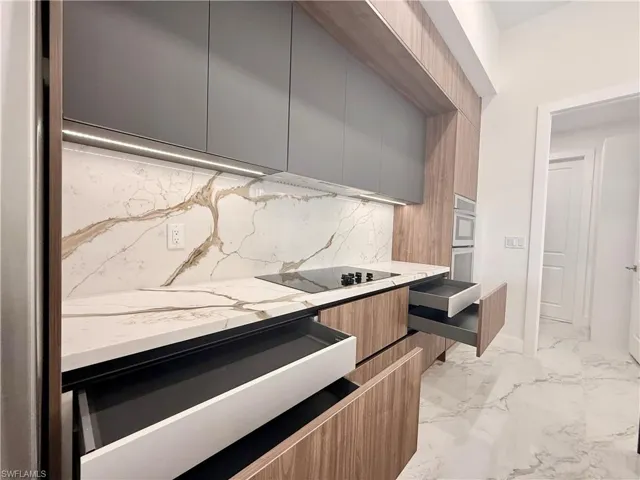 Kitchen with modern cabinets, decorative backsplash, black electric stovetop, light countertops, and light marble finish flooring