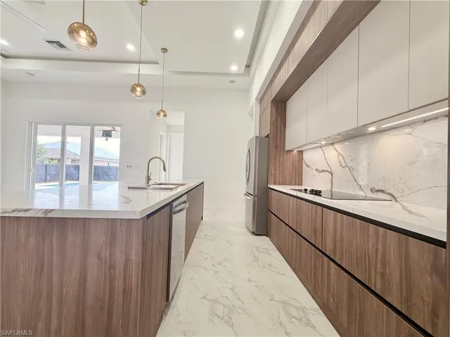 Kitchen featuring modern cabinets, appliances with stainless steel finishes, a raised ceiling, decorative backsplash, and recessed lighting