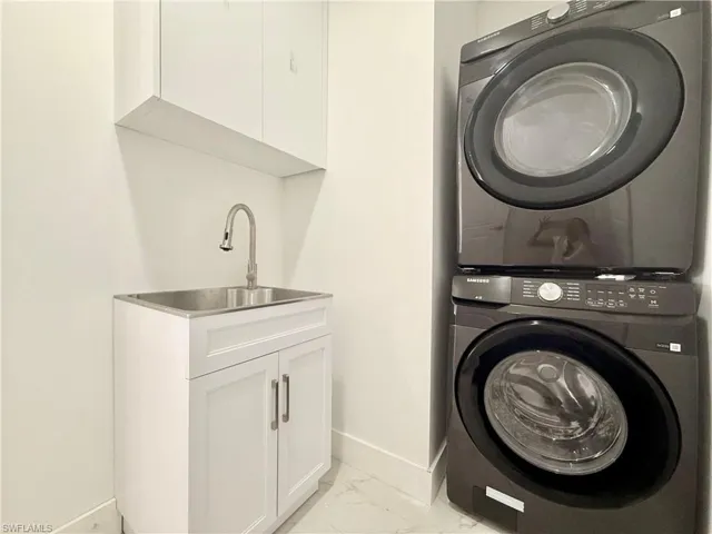 Washroom featuring stacked washer / drying machine, light marble finish floors, and cabinet space