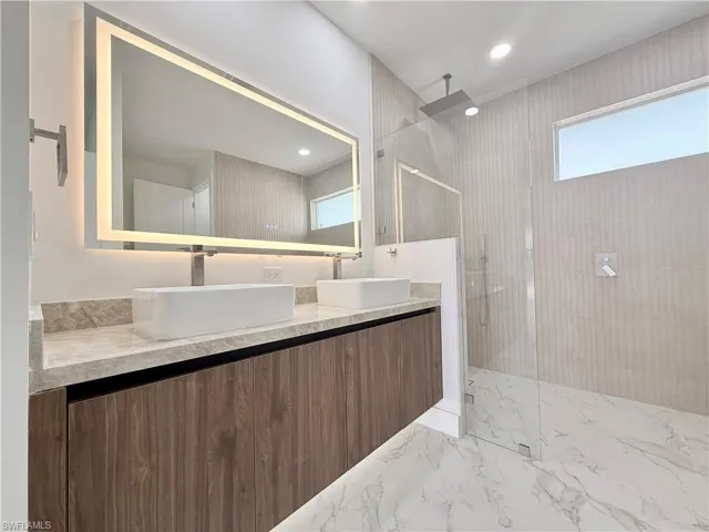 Full bathroom with double vanity, marble finish floors, and walk in shower