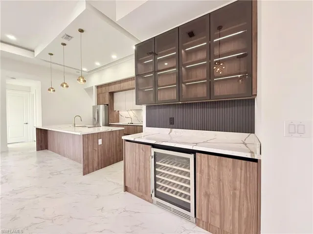 Kitchen with wine cooler, stainless steel fridge with ice dispenser, modern cabinets, a kitchen island with sink, and recessed lighting