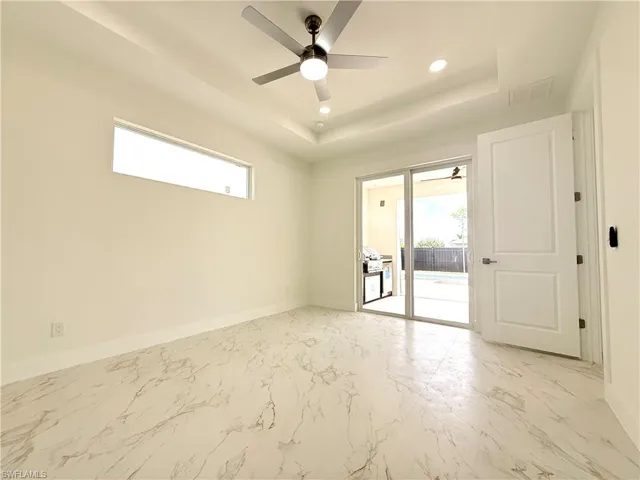 Unfurnished room with a raised ceiling, healthy amount of natural light, light marble finish floors, ceiling fan, and recessed lighting