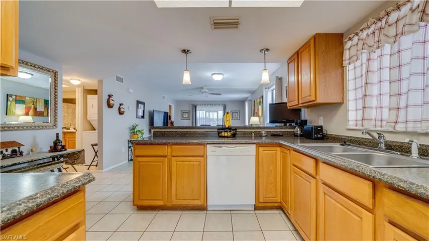 Kitchen featuring dishwasher, decorative light fixtures, light tile patterned flooring, a peninsula, and stacked washer / dryer