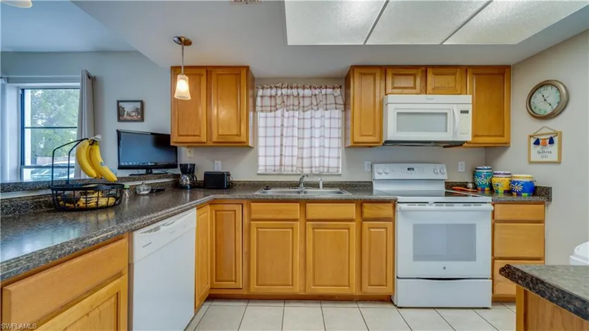 Kitchen featuring white appliances, dark countertops, brown cabinets, pendant lighting, and healthy amount of natural light