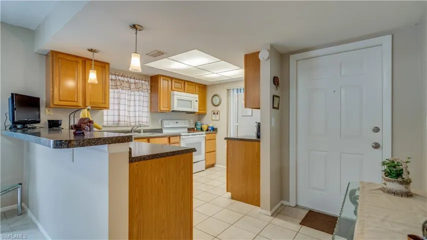 Kitchen with dark countertops, white appliances, a peninsula, and light tile patterned floors