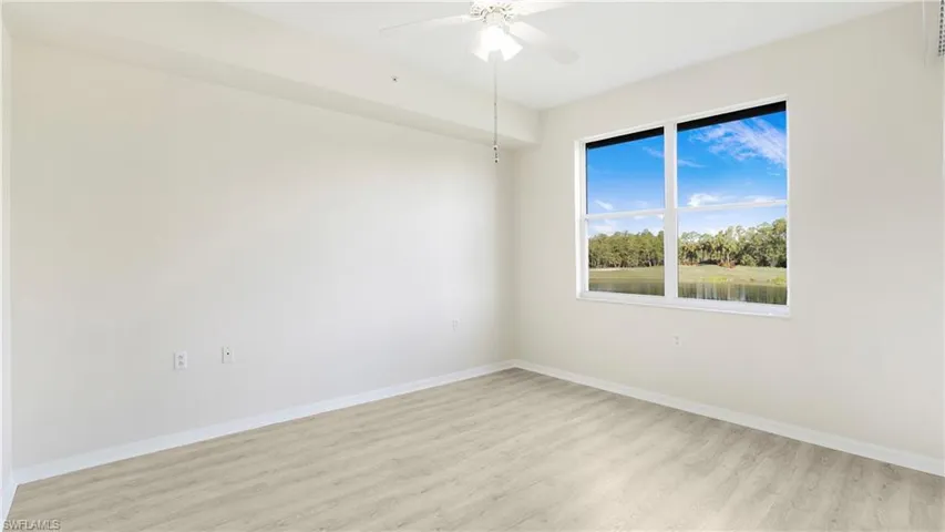 Empty room with light wood-type flooring, a water view, ceiling fan, and view of scattered trees