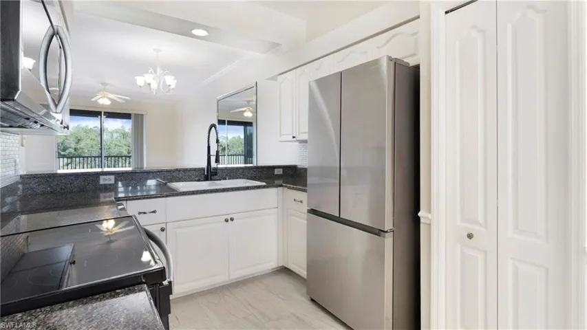 Kitchen with stainless steel appliances, white cabinets, dark stone counters, ornamental molding, and a chandelier