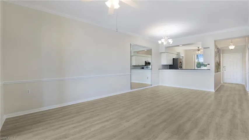 Unfurnished living room with a ceiling fan, light wood-style floors, crown molding, and a chandelier