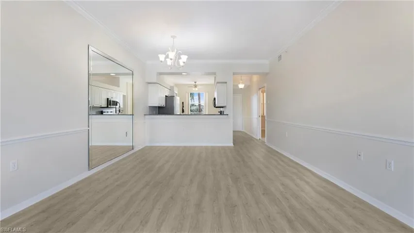 Unfurnished living room featuring light wood finished floors, crown molding, and a chandelier