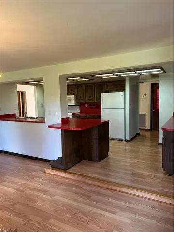 Kitchen with fridge, kitchen peninsula, dark brown cabinets, light wood-type flooring, and range