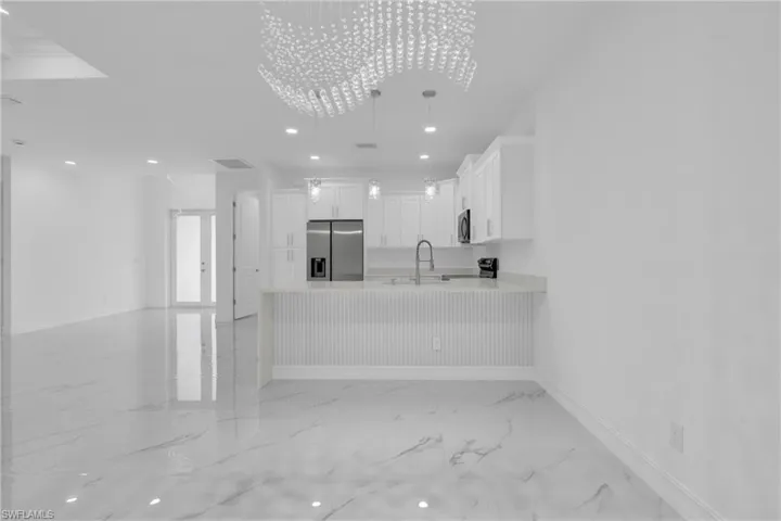Kitchen featuring recessed lighting, a peninsula, white cabinetry, light marble finish floors, and stainless steel appliances