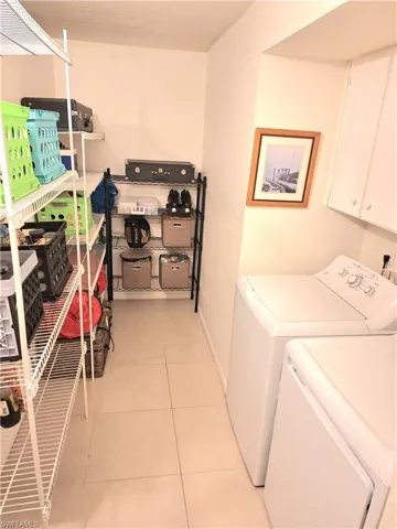Clothes washing area featuring washing machine and clothes dryer, cabinets, and light tile patterned floors
