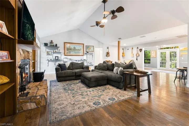 Living area with a ceiling fan, wood finished floors, french doors, high vaulted ceiling, and a stone fireplace