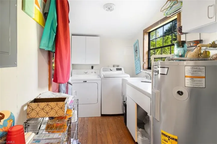 Washroom featuring water heater, washing machine and dryer, cabinet space, wood finished floors, and electric panel