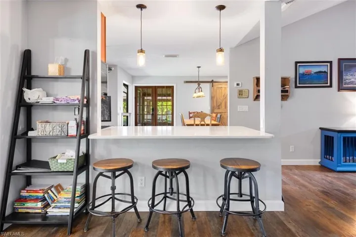 Kitchen with dark wood-style floors, a kitchen breakfast bar, decorative light fixtures, baseboards, and a peninsula