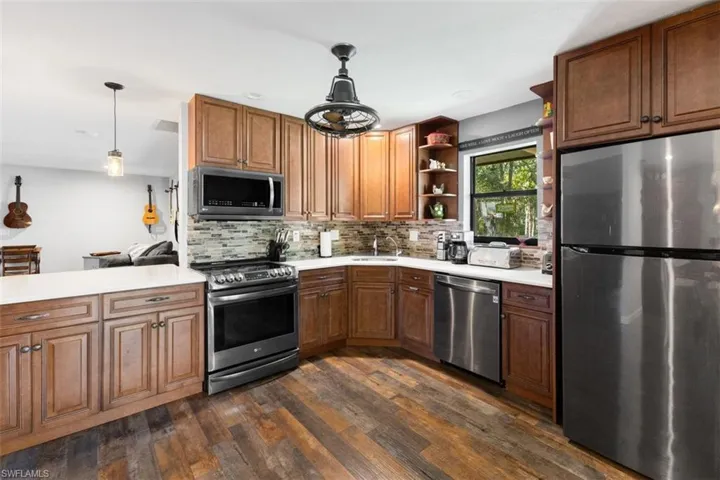 Kitchen with appliances with stainless steel finishes, open shelves, dark wood-style floors, backsplash, and light countertops