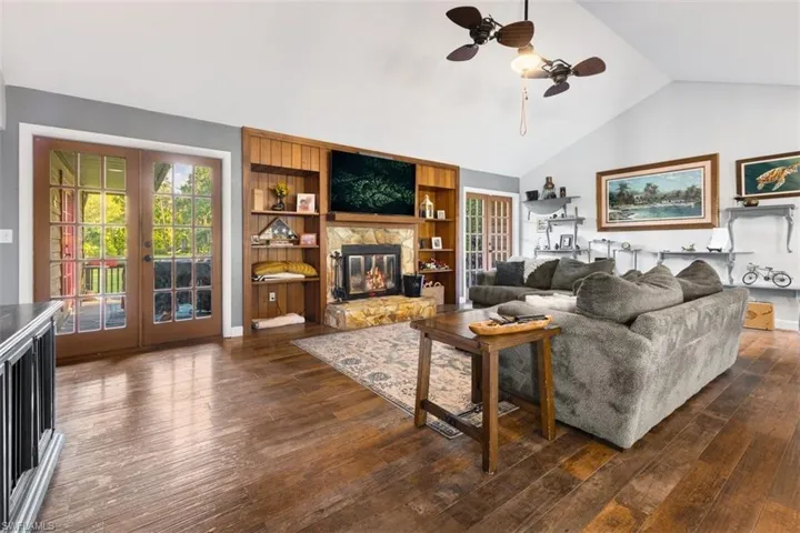 Living area featuring french doors, dark wood-style flooring, ceiling fan, high vaulted ceiling, and a stone fireplace