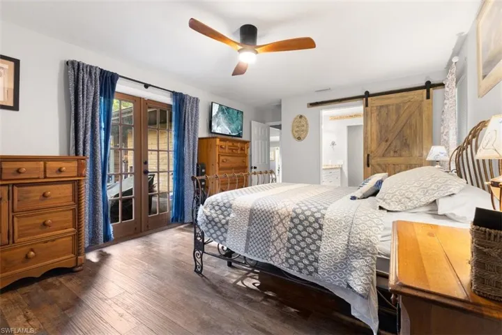 Bedroom featuring a barn door, wood finished floors, french doors, access to outside, and ensuite bathroom