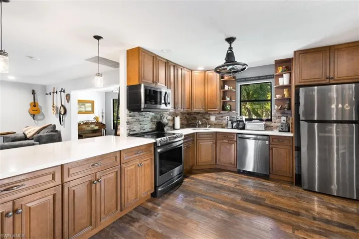 Kitchen featuring appliances with stainless steel finishes, open shelves, a sink, tasteful backsplash, and dark wood-style flooring