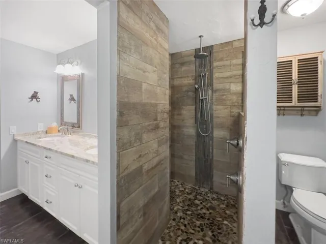 Full bath with toilet, double vanity, walk in shower, baseboards, and wood finished floors