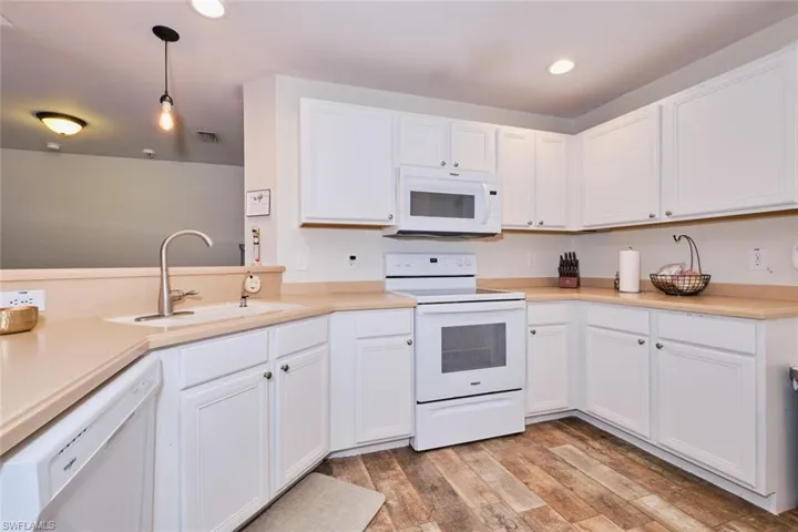 Kitchen featuring decorative light fixtures, light wood-type flooring, white cabinets, sink, and white appliances