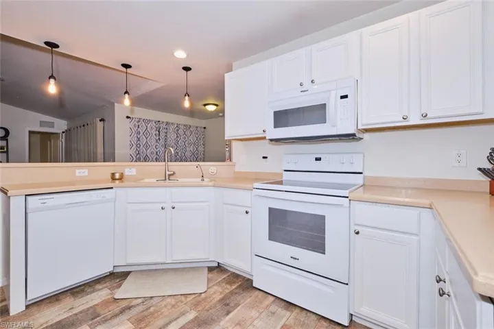 Kitchen with light wood-type flooring, white appliances, white cabinets, pendant lighting, and sink