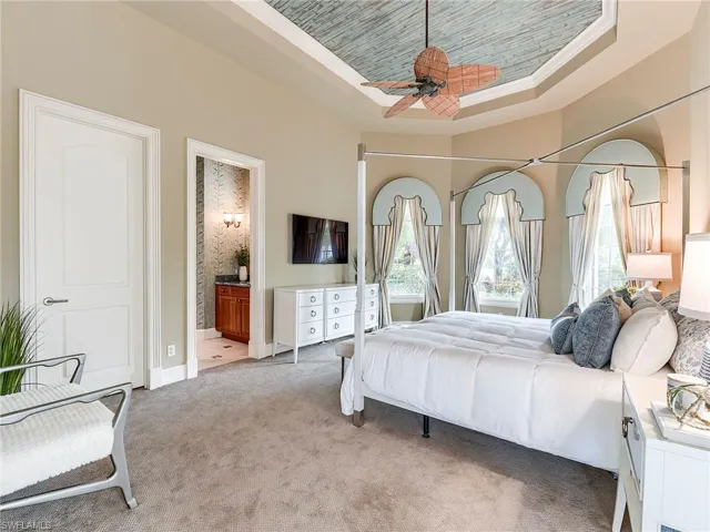 Ground level bedroom with a raised ceiling, light colored carpet, ensuite bath, and a ceiling fan, includes en-suite.