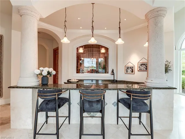Bar area featuring decorative columns, dark stone counters, hanging light fixtures, and crown molding
