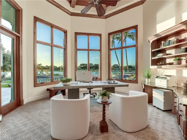 Office with light colored carpet, a ceiling fan, a towering ceiling, coffered ceiling, and beam ceiling