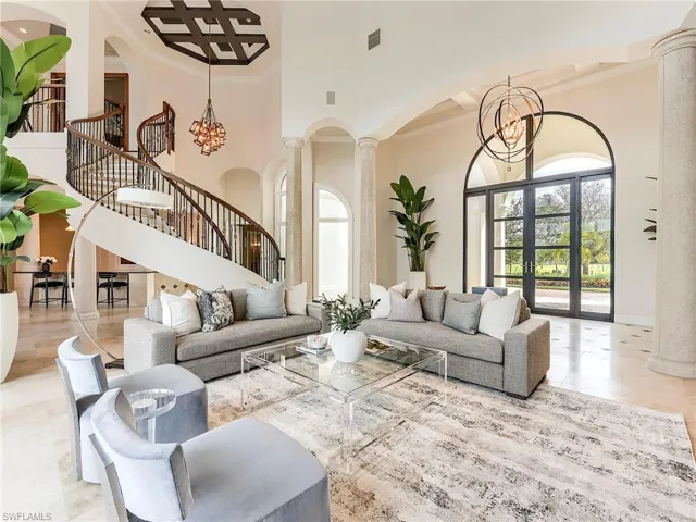 Living room with a chandelier, a towering ceiling, ornate columns, ornamental molding, and french doors