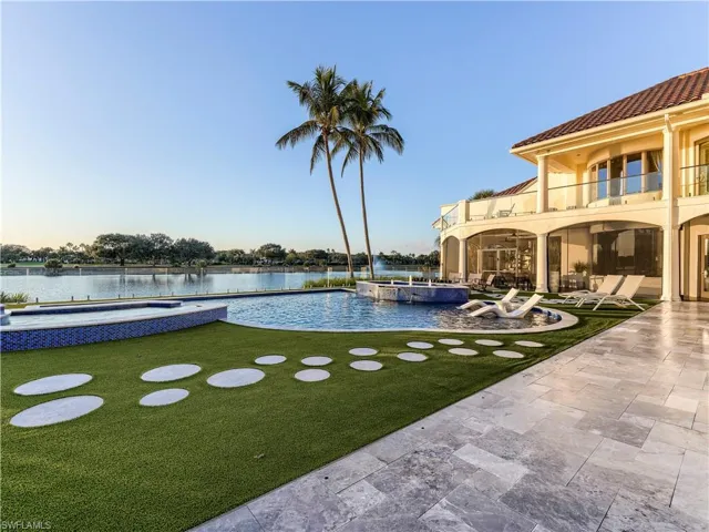 View of green lawn with a pool with connected hot tub, a balcony, a patio, and a water view